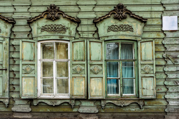 two windows with the wooden carved architrave in the old wooden house in the old Russian town.