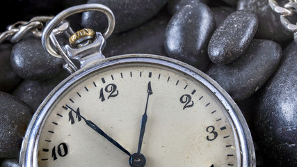 An antique gold pocket watch lies on a pile or small rocks.