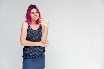 Portrait to the waist of a young pretty girl teenager in a T-shirt and skirt with beautiful purple hair on a white background in the studio. Talking, smiling, showing hands with emotions.