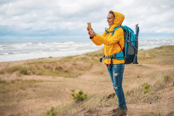 happy young beautiful woman in yellow jacket hiking backpack phone on the North Sea