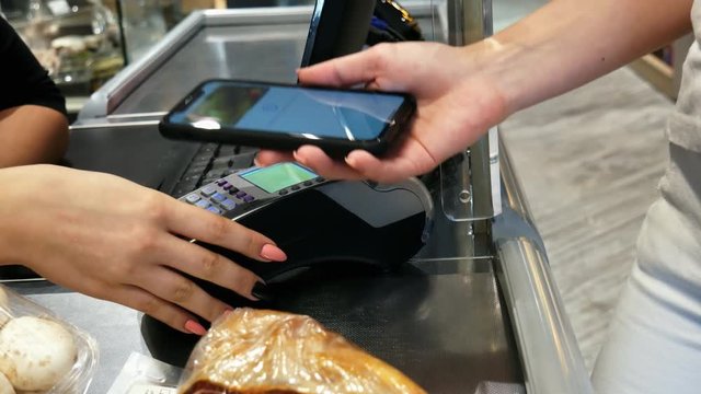 Woman pays for purchases in the supermarket terminal at the checkout using contactless payment through the phone