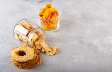 Apple, pineapple and mango chips in a jar and pieces of this fruits on a table