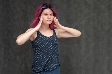 Portrait to the waist of a young pretty girl teenager in a T-shirt with beautiful purple hair on a gray background in the studio. Talking, smiling, showing hands with emotions.