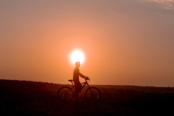 Obraz premium Happy girl with a bicycle on the nature on the background of bright sunset and yellow sun