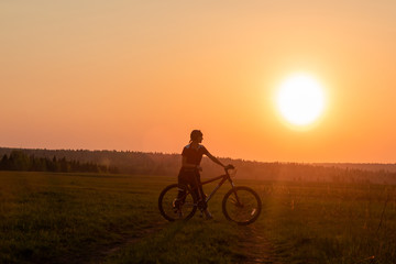 Fototapeta na wymiar Happy girl with a bicycle on the nature on the background of bright sunset and yellow sun