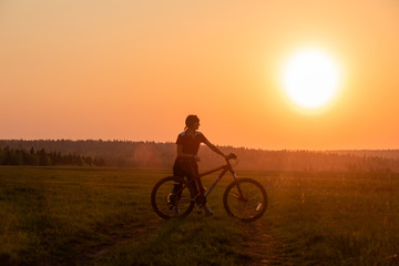 Fototapeta na wymiar Happy girl with a bicycle on the nature on the background of bright sunset and yellow sun