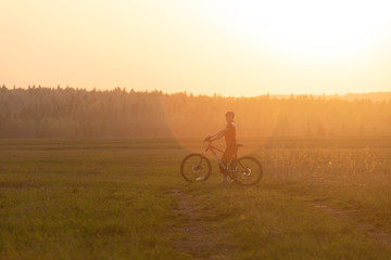 Obraz premium A girl rides a bicycle on the road against the backdrop of a bright sunset and yellow sun
