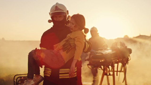 Brave Firefighter Carries Injured Young Girl to Safety. In the Background Car Crash Traffice Accident with Courageous Paramedics and Firemen Save Lifes, Fight Fire