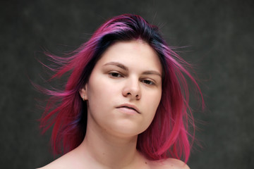 Close-up portrait of a young pretty teen girl with beautiful purple hair on a gray background in the studio. Smiles with emotions