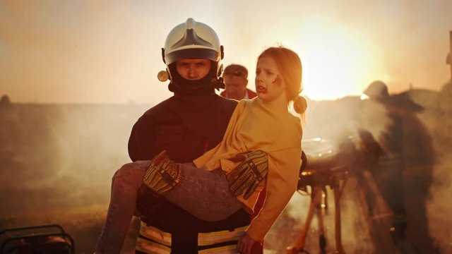 Brave Firefighter Carries Injured Young Girl to Safety. In the Background Car Crash Traffice Accident with Courageous Paramedics and Firemen Save Lifes, Fight Fire