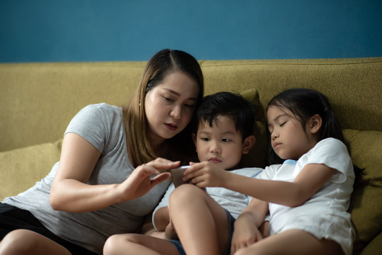 Parent Homeschooling - Happy Asian Family , Mother Looking a Smartphone with Daughter and Son in Living Room for Relax and Teaching Children