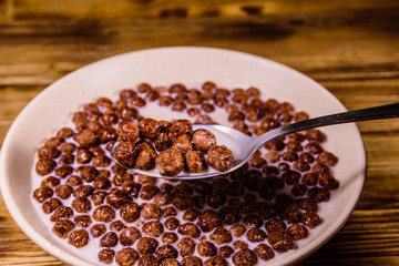Ceramic plate with chocolate cereal balls in milk on wooden table