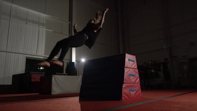 Female athlete doing impressive tumbling on trampolines and gym parcour equipment