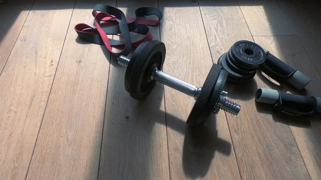 Fitness equipment lying unused in time lapse on the wooden floor. The afternooFitness equipment lying unused in time lapse on the wooden floor. The afternoon passesn passes and the shadows get longer.