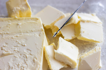 Bowl with cubes of butter and greens on table. Cut the cubes of butter with a knife. Cut butter with a knife. Cut butter with black knife. Cut butter. Cubes of cut butter