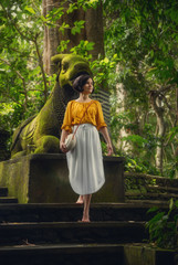 Girl in the Monkey Forest. Bali. Girl in a white dress on the nature. Traditional Balinese bag. Travel.	