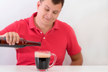 Happy man pouring a dark beer into a mug from a glass bottle