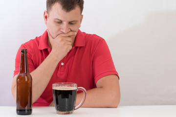 man sitting at a table with a mug of beer, struggling with alcohol addiction