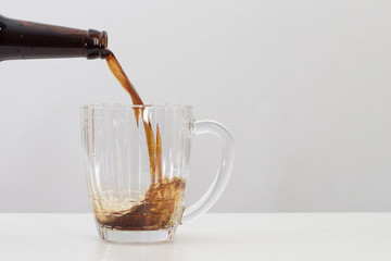 dark beer is poured into a glass bottle mug, white table and background, copy space
