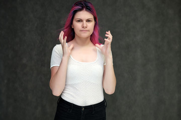 Portrait to waist of a young beautiful girl teenager in a white T-shirt with beautiful purple hair on a gray background in the studio. They say, they smile, they show hands with emotions.