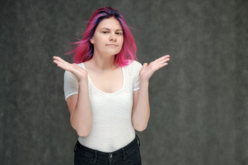 Portrait to waist of a young beautiful girl teenager in a white T-shirt with beautiful purple hair on a gray background in the studio. They say, they smile, they show hands with emotions.