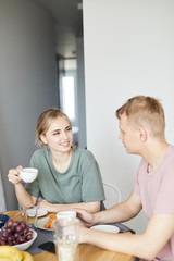 Pretty young woman talking to her husband by cup of tea by breakfast in the morning