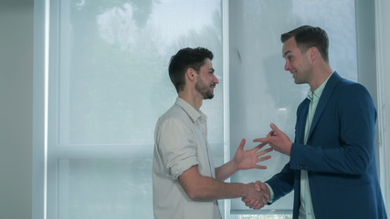 Businessmen near the windows meeting. Smiling happy man talking with mixed race laughing guy.