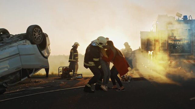 Brave Firefighter Carries Injured Young Girl to Safety where She Reunited with Her Loving Mother. In the Background Car Crash Traffic Accident Courageous Paramedics and Firemen Save Lives