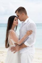 Newlyweds are hugging on a gorgeous beach with white sand and turquoise water.