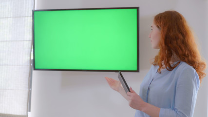 Redheaded manager standing near display with green screen on the wall. Businesswoman holding...