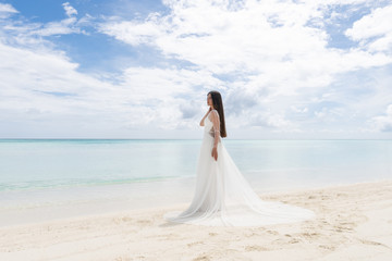 Fototapeta na wymiar The perfect bride. A young bride in a white dress is standing on a snow-white beach.
