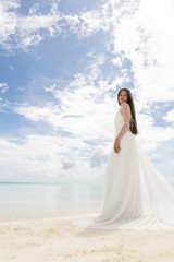 Fototapeta na wymiar The perfect bride. A young bride in a white dress is standing on a snow-white beach.