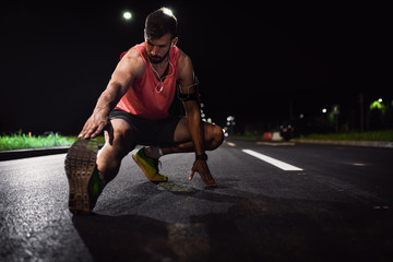 Man preparing to run through the city at night, he stretching his leg muscles.