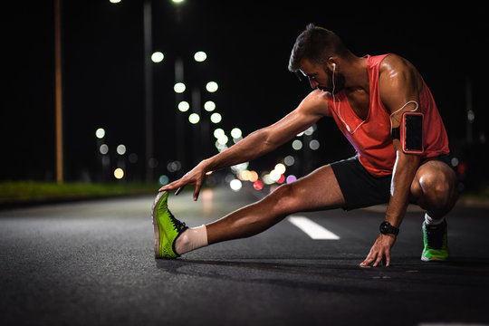 Man preparing to run through the city at night, he stretching his leg muscles.
