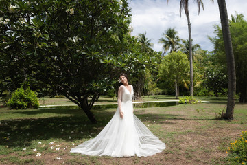 A bride in a white dress with an exotic flower in her hair is standing under a flowering tropical tree.