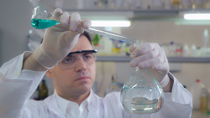 Handsome professional scientist using medical equipment holding flasks with liquid in medical or...