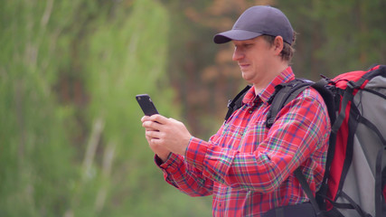 Portrait man hiker using smartphone typing message of surfing internet in forest. Caucasian young man hiking enjoy nature in summer season. Handsome backpacker holding mobile phone texting with happy