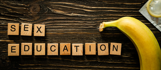 Sex education concept - letters, banana and condoms on wood background, top view