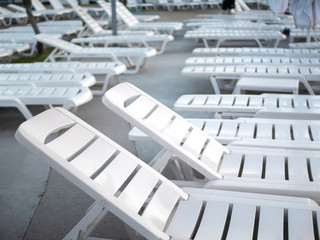 Lots of white empty sun loungers at the pool closeup at sunset