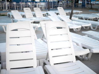 Lots of white empty sun loungers at the pool closeup at sunset