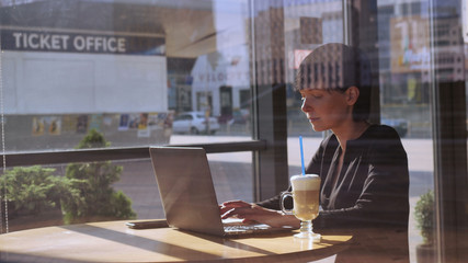 Elegant professional businesswoman using internet for working with document in cafe. Busy adult caucasian woman has coffee break in coffeehouse typing on computer in daytime.