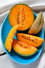 Ripe and fresh cantaloupe melon. Bright orange fruit on a blue ceramic plate. Perfect food for hot summer party, delicious dessert. Cut in pieces, ready for eating, served cold