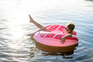 Girl in a pink bathing suit and sunglasses swimming on an inflatable ring, a copy of the free space.