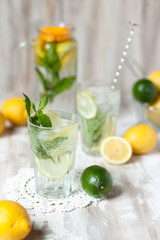 Summer composition with refreshing healthy alcohol free home made lemonade with pepper mint, limes and lemons. White lace napkin as decor, wooden background. Vacation mood, enjoying summertime