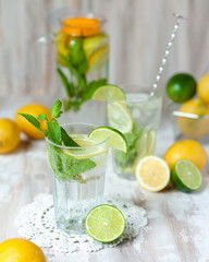 Summer composition with refreshing healthy alcohol free home made lemonade with pepper mint, limes and lemons. White lace napkin as decor, wooden background. Vacation mood, enjoying summertime