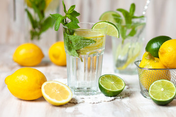 Summer composition with refreshing healthy alcohol free home made lemonade with pepper mint, limes and lemons. White lace napkin as decor, wooden background. Vacation mood, enjoying summertime