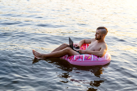Workaholic man working on a laptop while sitting on an inflatable ring, copy space.