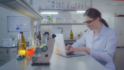 Portrait adult caucasian doctor working with laptop in laboratory. Chemist engineer or lab technician entering data on laptop. Professional woman working in the evening alone.
