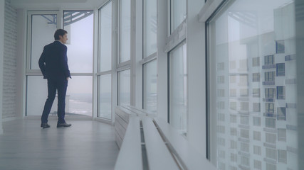 handsome professional businessman celebrating victory. Successful man walking in empty modern room. Guy standing near big windows and enjoy view.