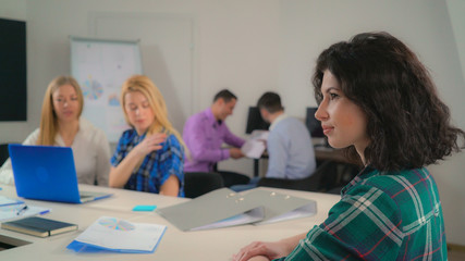 Portrait attractive woman with curly black hair in office startup company. Young businesswoman looking at the camera with friendly smile. Professional female with natural makeup smiling. On the